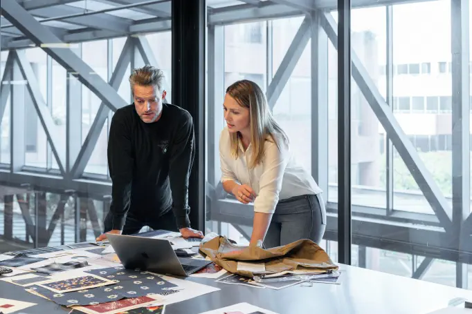 Two colleagues reviewing forecast figures together at a desk by tall office windows