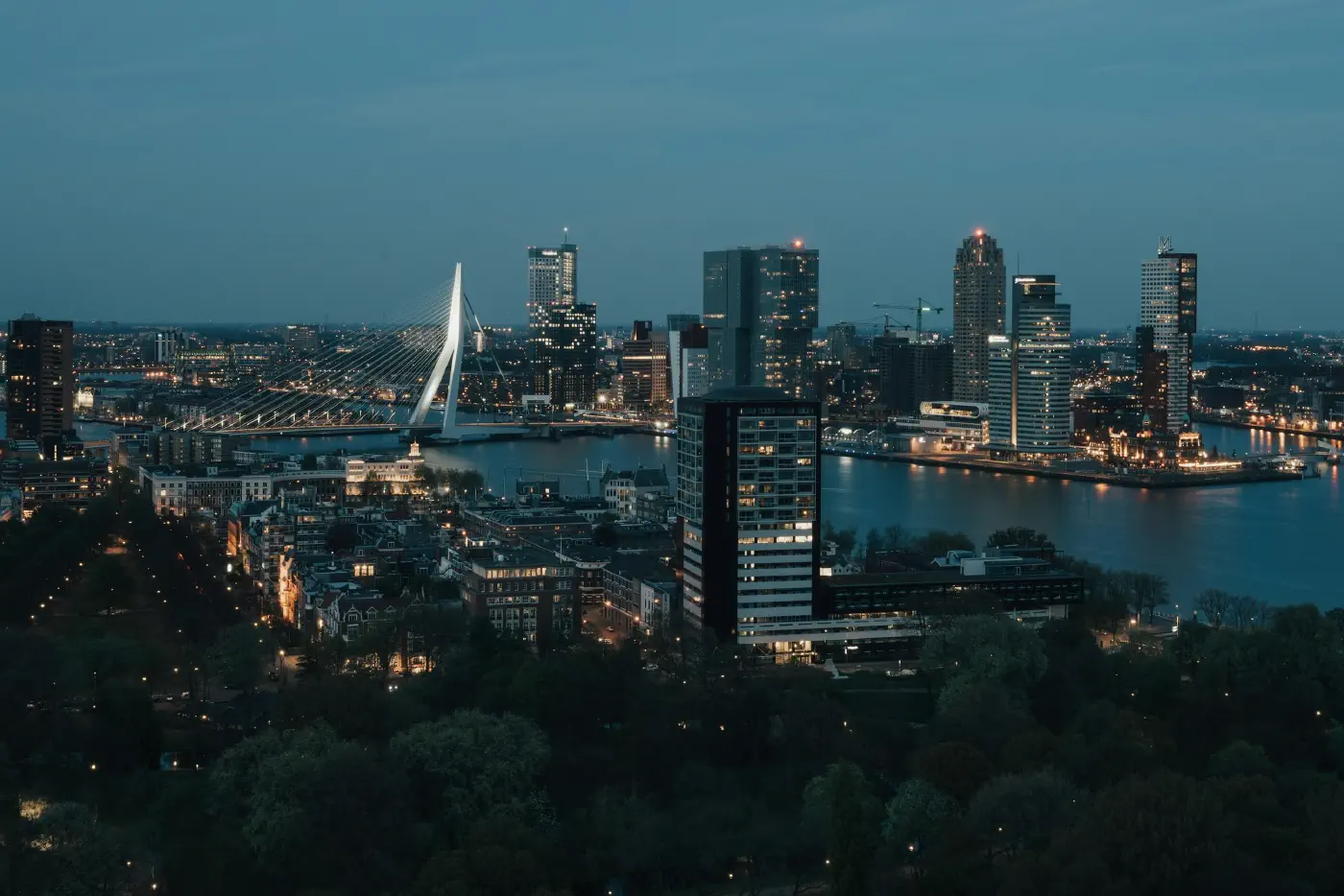 Aerial view over Rotterdam at dusk, high-rise towers, low-rise streets and the river in one frame, the different kinds of site a city holds.